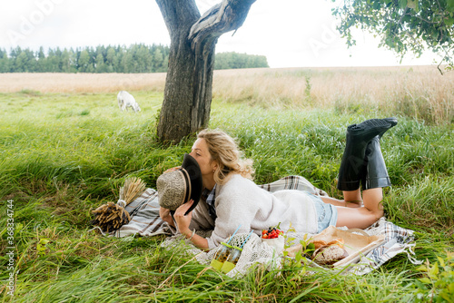 A cute girl in a hat and black rubber boots sits on a plaid. picnic in the park outdoors. summer in the village. fresh fruits and berries, cake and bread photo