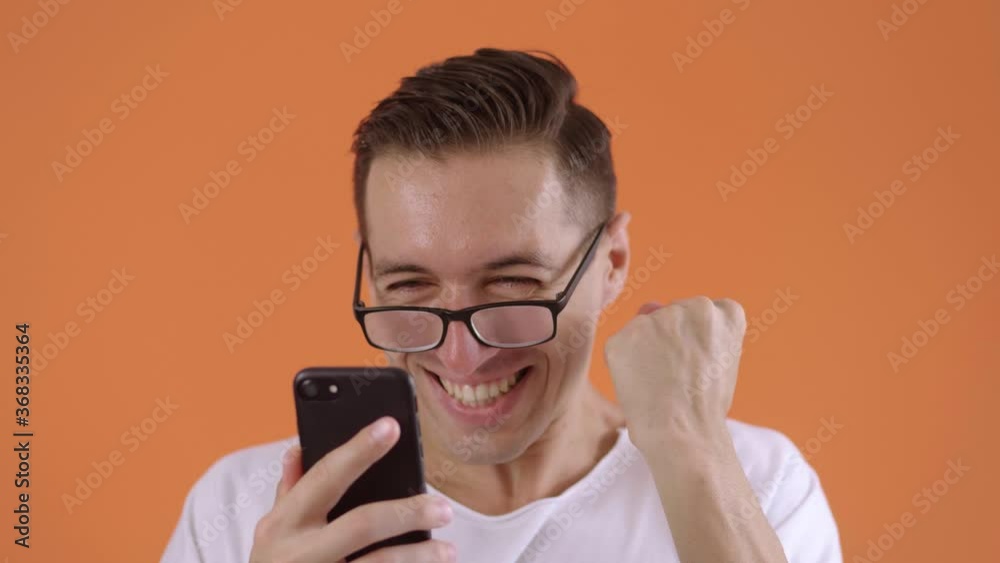 Excited hipster man in surprise shoots glasses celebrating success in studio on orange background. Portrait of happy person shoots glasses and showing yes gesture. Excited hipster man in surprise shoots glasses celebrating success in studio on orange background. Portrait of happy person shoots glasses and showing yes gesture.