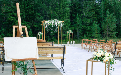 Wedding decor of ceremony outdoors in forest, welcome board, coasters for flowers and elegant floral decoration of arch