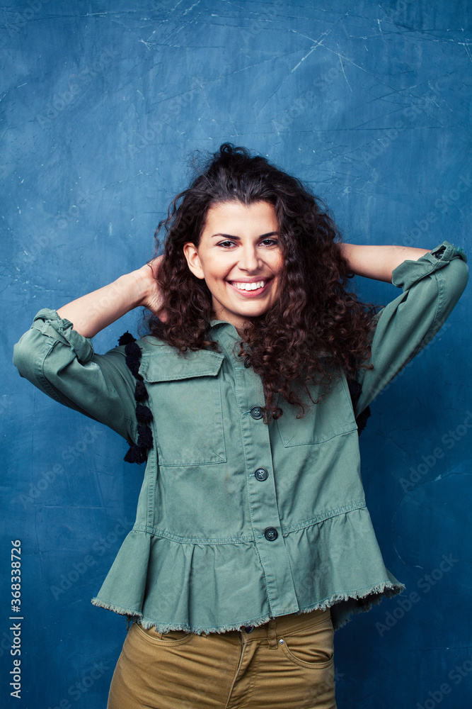 young pretty woman with curly brunette hair posing cheerful on blue background, lifestyle people concept young pretty woman with curly brunette hair posing cheerful on blue background, lifestyle people concept