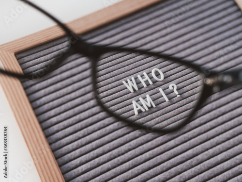 Top view on letterboard with words WHO AM I through eyeglasses. Flat lay concept of psychological self-regulation or gender identity. Social psychological issue. Closer look on psychological problems. photo