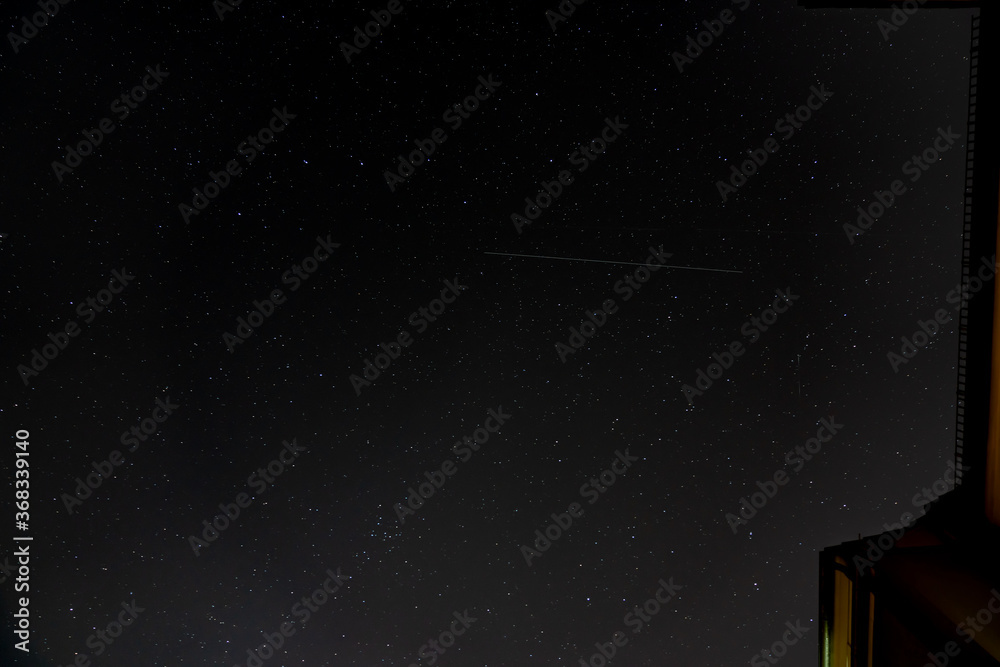 Starlink communication satellite trail crossing starry sky above city houses Starlink communication satellite trail crossing starry sky above city houses
