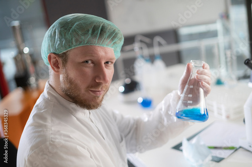 A male chemist agitating a beaker of blue liquid in a lab.