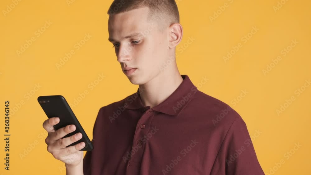 Attractive casual blond guy intently using smartphone and smiling over colorful background Attractive casual blond guy intently using smartphone and smiling over colorful background