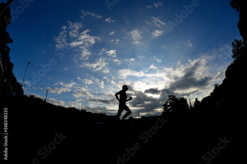 Ein Sportler läuft auf der Laufbahn in einem Stadion und bildet sich als Silhouette vor dem Morgenhimmel ab.