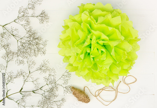 Light green fluffy pom-pom from tissue paper on a white wooden table background. Top view. photo