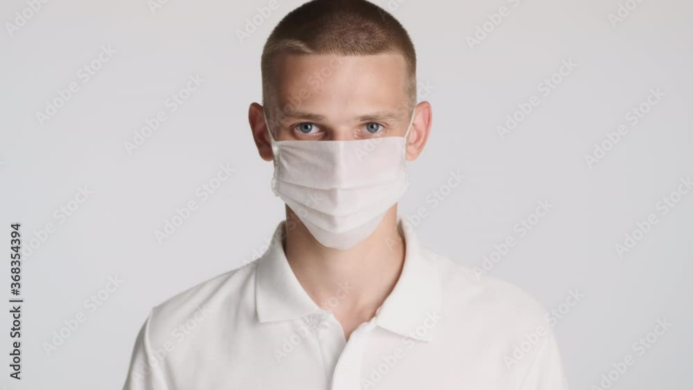 Young casual man in medical mask intently looking in camera over white background. Safety concept Young casual man in medical mask intently looking in camera over white background. Safety concept