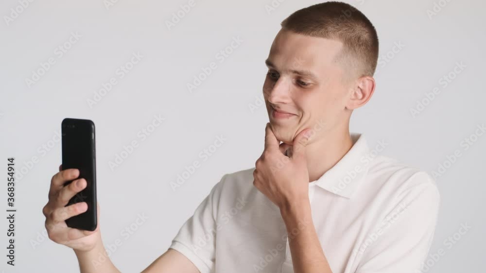 Young handsome smiling man having video call happily talking with friends on smartphone over white background Young handsome smiling man having video call happily talking with friends on smartphone over white background