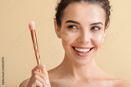 Fototapete Beautiful young woman with foundation on her face against color background