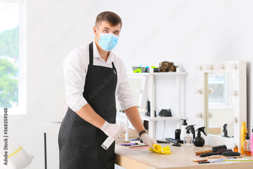 Male hairdresser cleaning workplace in salon during coronavirus
