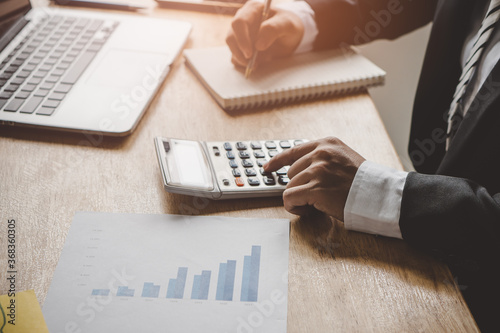 Businessman counting on calculator and reviewing budget on business plan.