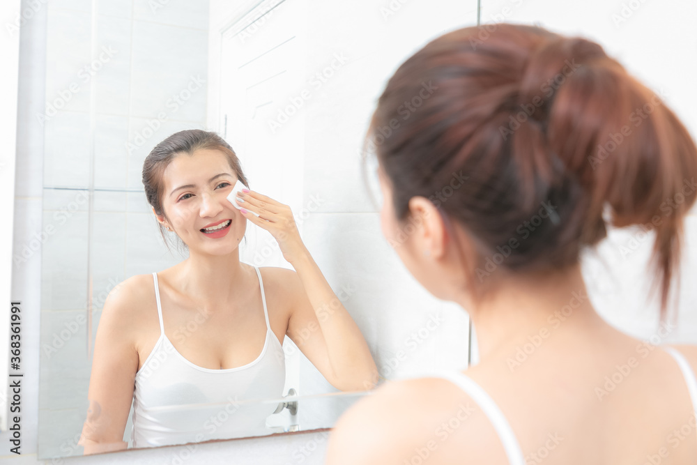Beautiful Asian Woman applying cosmetic cream in bathroom.