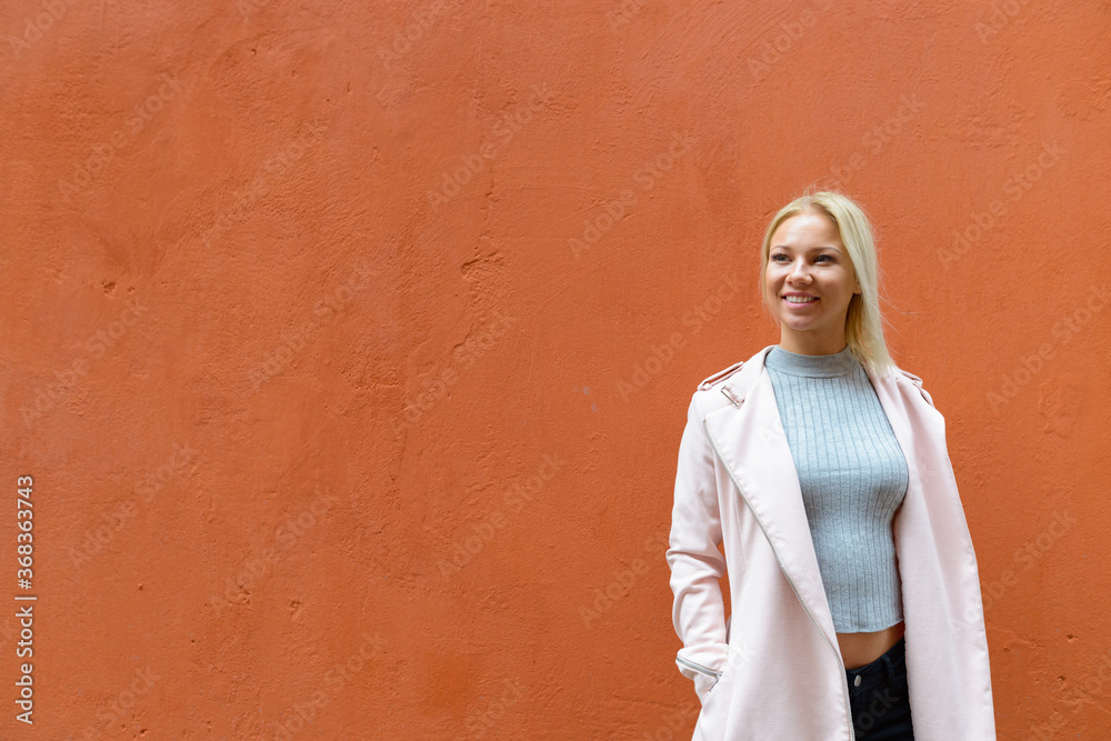 Happy young beautiful blonde woman thinking against orange wall outdoors Happy young beautiful blonde woman thinking against orange wall outdoors