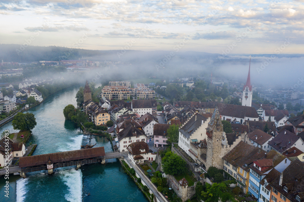 medieval town by the river with wooden bridge in the morning fog