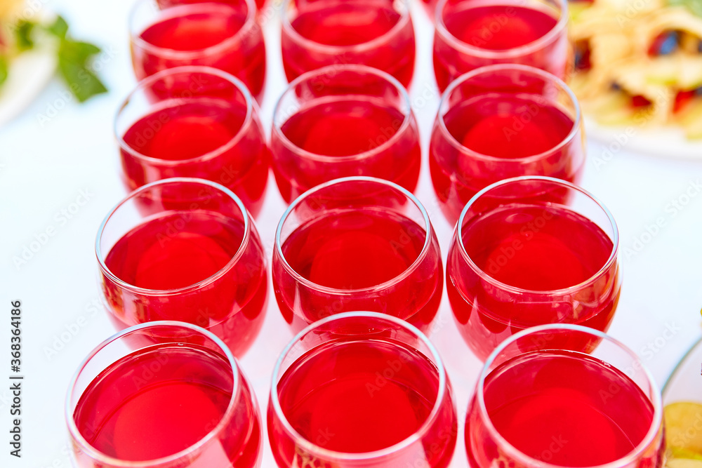 A row of glasses with red drinks, juice, champagne or wine at a party. Catering. Glassware on the table with a white tablecloth. Festive buffet for the holiday. A row of glasses with red drinks, juice, champagne or wine at a party. Catering. Glassware on the table with a white tablecloth. Festive buffet for the holiday.