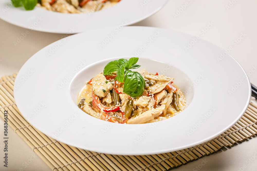Close-up chicken with vegetables in sesame sauce in a white plate on a plain background. Traditional Thai food. Close-up chicken with vegetables in sesame sauce in a white plate on a plain background. Traditional Thai food.