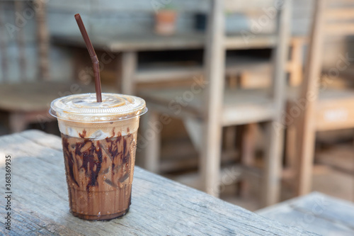 close up shot with blurred background of iced beverage (chocolate, cocoa, mocha coffee) in clear plastic cup put on the vintage wooden table. It looks delicious for drinking cool dessert in summer