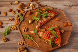 close up image of  vegetarian cheese and tomato pizza decorated with fresh arugula leaves and grilled egg plants slices. It is served on wooden tray with hazelnuts, almonds and walnuts