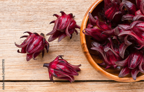 Closeup fresh red  Roselle fruit ( Jamaica sorrel, Rozelle or hibiscus sabdariffa ) in wooden bowl  isolated on wooden table background. Top view.