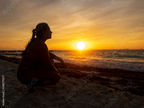 silhouette of kneel woman looking orange sunset at beach