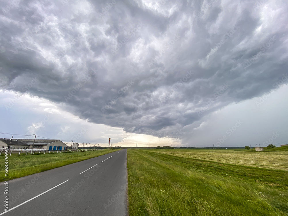 empty asphalt road through the countryside farmland with dark and foreboding storm clouds on the horizon empty asphalt road through the countryside farmland with dark and foreboding storm clouds on the horizon