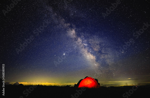 The orange tent under the beautiful starry sky glows at night. The orange tent under the Milky way at night.