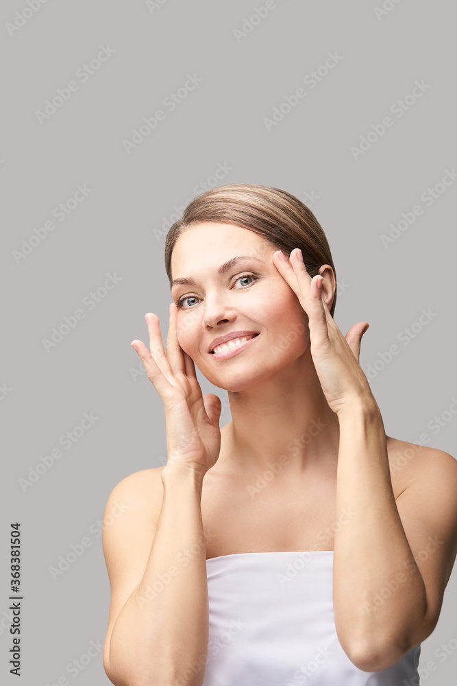 Happy pretty woman. Hands near face. Skincare concept. Home morning routine. Clean skin. Cream cosmetics. Cosmetology therapy. Rejuvenation procedure. Grey background. Copyspace Happy pretty woman. Hands near face. Skincare concept. Home morning routine. Clean skin. Cream cosmetics. Cosmetology therapy. Rejuvenation procedure. Grey background. Copyspace