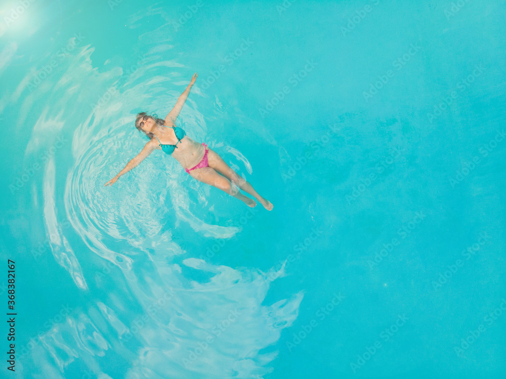 Aerial view of a relaxed young woman in the transparent turquoise sea. Top view of slim woman relaxing in hotel pool.