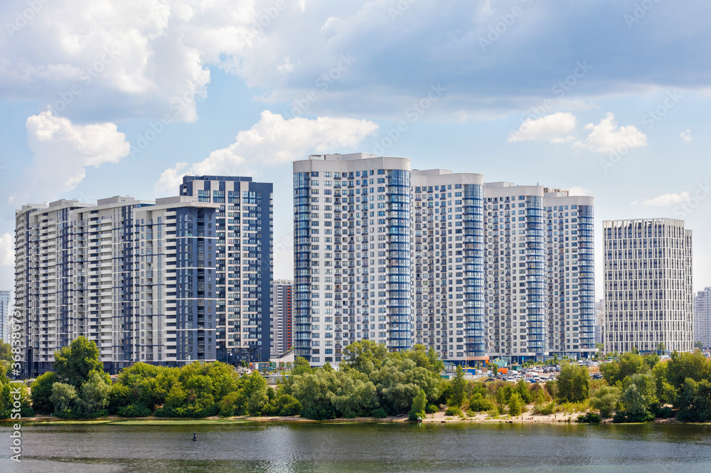 The facades of new residential high-rise buildings on the banks of the river and against the blue cloudy sky. The facades of new residential high-rise buildings on the banks of the river and against the blue cloudy sky.