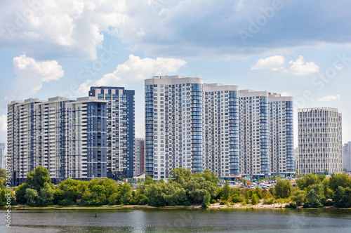 The facades of new residential high-rise buildings on the banks of the river and against the blue cloudy sky. © Sergii