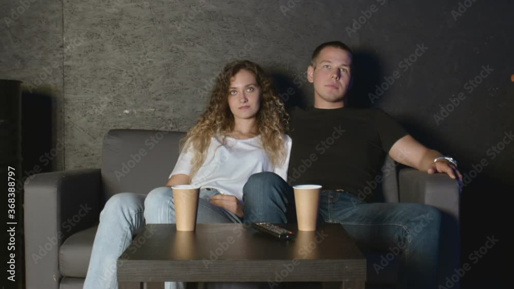 A couple of lovers watch television embraced on the sofa. watch a movie together. A couple of lovers watch television embraced on the sofa. watch a movie together.
