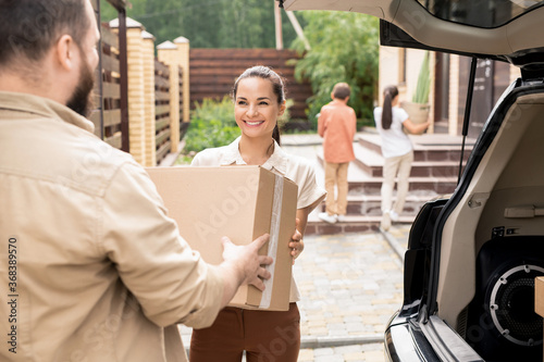 Photos Over shoulder view of man passing moving box to wife while unloading car during