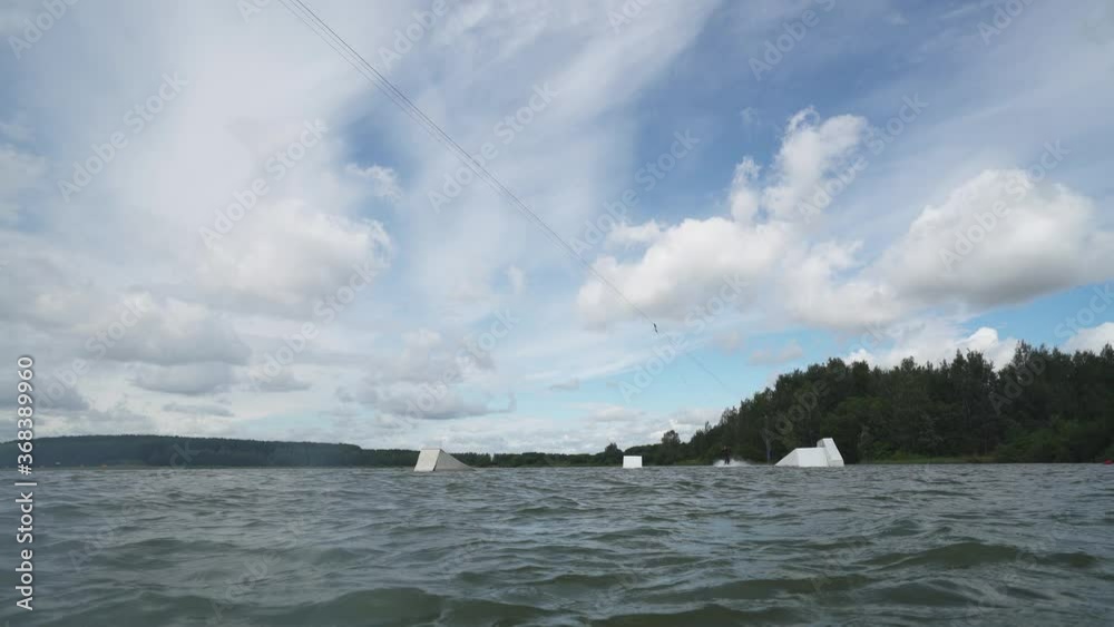 Wakeboarding in a lake near the forest, adult man surfs on the water, ride on a wakeboarding board and performs tricks, jumps on a springboard. Wakeboarding in a lake near the forest, adult man surfs on the water, ride on a wakeboarding board and performs tricks, jumps on a springboard.