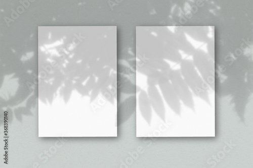 2 vertical sheets of textured white paper on soft gray table background. Mockup overlay with the plant shadows. Natural light casts shadows from an exotic plant. Horizontal orientation