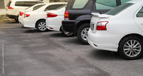 Closeup of rear, back side white car with other cars parking in outdoor parking area.