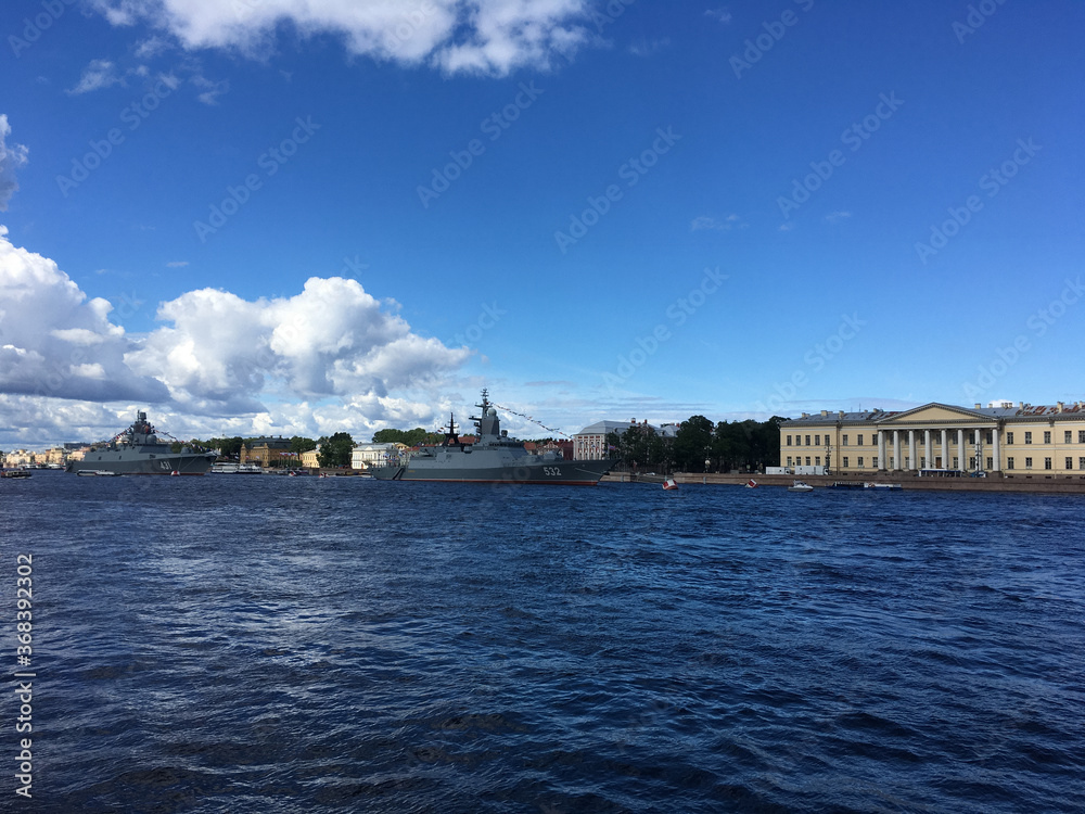 Neva water area with warships arriving to participate in the naval parade, taking place in St. Petersburg against the backdrop of attractions and blue sky with clouds.