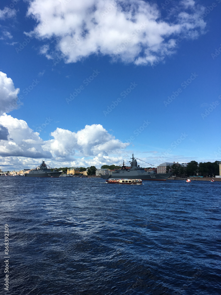 Warships in the water area of ​​the Neva, arrived to participate in the naval parade in St. Petersburg, near pleasure boats with tourists.