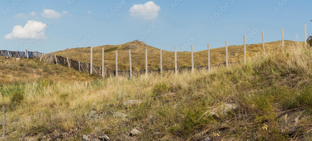 Summer steppe landscape. Landscape in kazakhstan. Kazakh steppe. Blue sky. Yellow grass. Panorama. Concrete pillars and fence. Hills