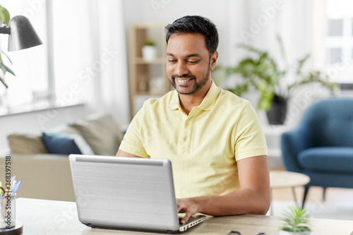 technology, remote job and lifestyle concept - happy smiling indian man with laptop computer working at home office