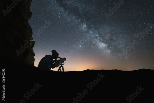 milky way in the sky and person looking through telescope