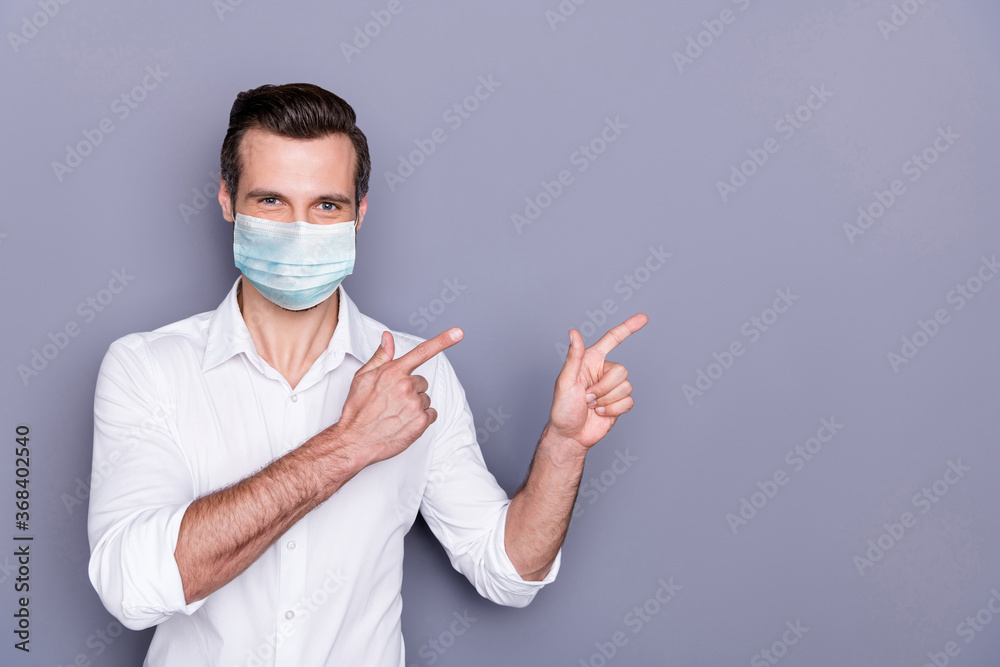 Portrait of his he attractive healthy guy wearing safety gauze mask demonstrating copy space placard poster stop infection influenza pandemia health care isolated gray color background