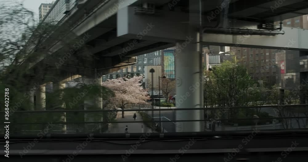 Tokyo urban industrial view with cherry blossoms from subway train window. Modern buildings and highway, bridge and river at spring.