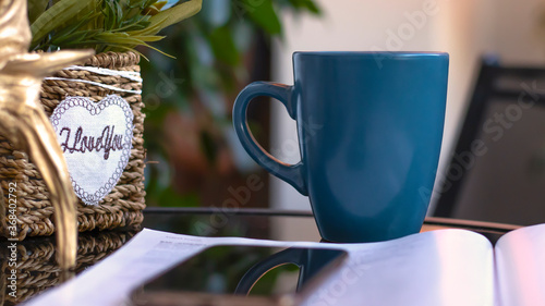 Evening coffee. Blue cup with coffee, open book and mobile phone, evening light, sunset, dusk. Atmospheric, cozy evening in the garden, green leaves, conversation. Warm light, blur bokeh.