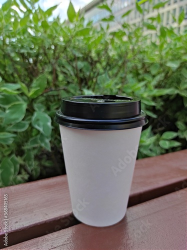 White paper coffee cup disposable for take away or to go, at wooden table and green nature background, copy space for text or logo. Street coffee, top view.