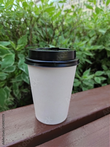 White paper coffee cup disposable for take away or to go, at wooden table and green nature background, copy space for text or logo. Street coffee, top view.