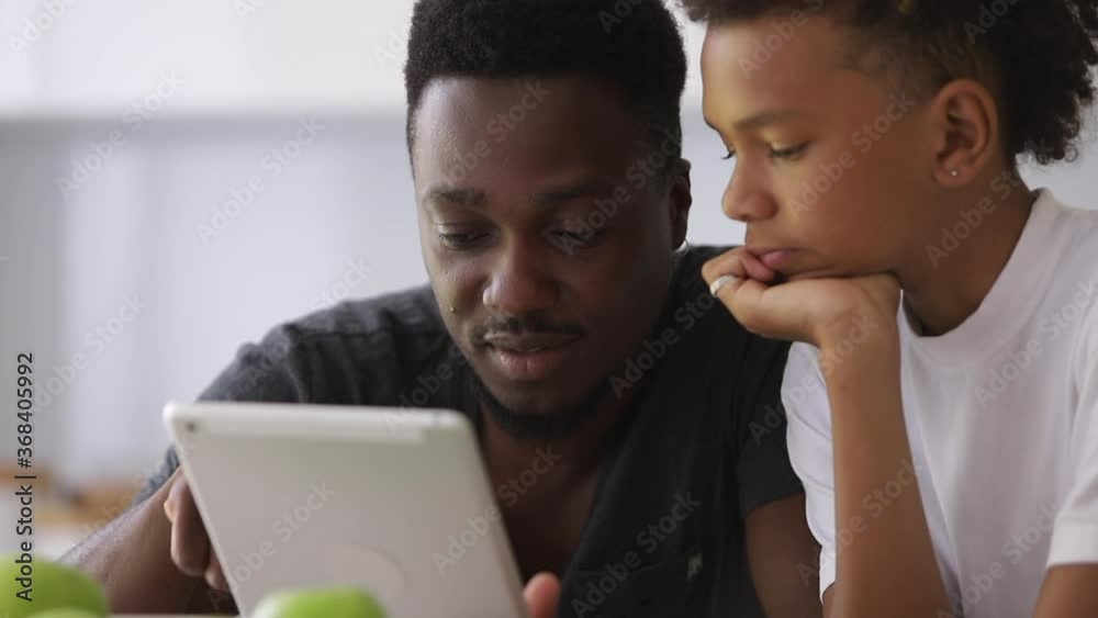 afro father educating son, showing him information on tablet Spbi. family communication and bonding. scrolling touchscreen and explaining game. concept parenthood afro father educating son, showing him information on tablet Spbi. family communication and bonding. scrolling touchscreen and explaining game. concept parenthood