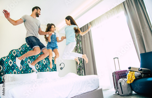 Funny and excited family are having fun, jumping and playing together on the bed in a big room