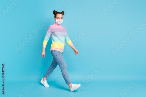 Fototapeta Naklejka Na Ścianę i Meble -  Full size profile photo of pretty teen lady keep social distance walk down street quarantine time wear protect face mask jeans striped pullover shoes isolated blue color background