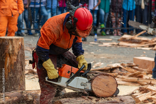 man cutting a log with chainsaw in safety outfit exhibition