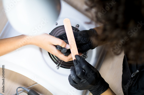 manicurist master in black mask and gloves making manicure for a client with a nailfile photo